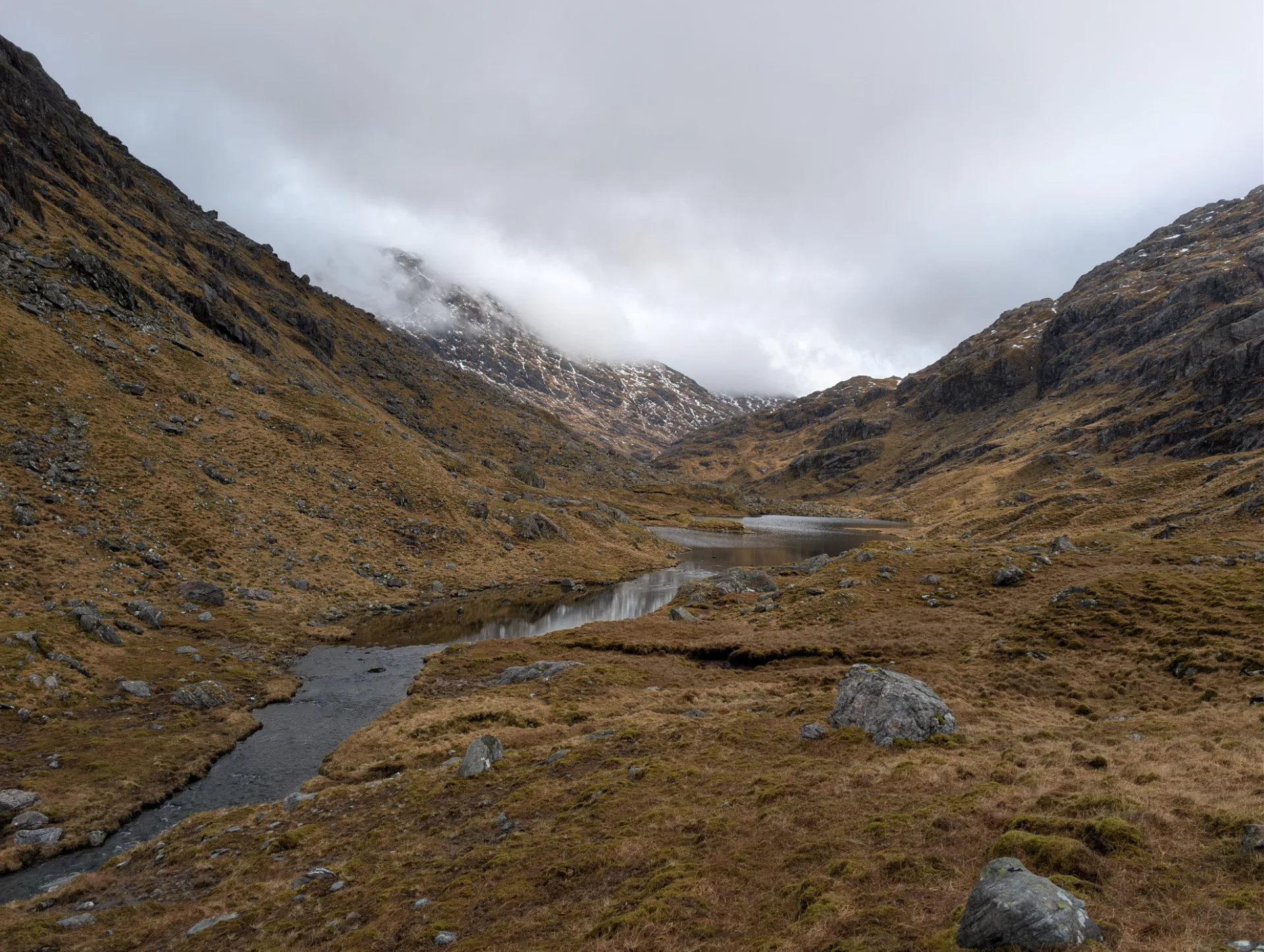 Small mountain loch in the valley, clouds clinging to the slope