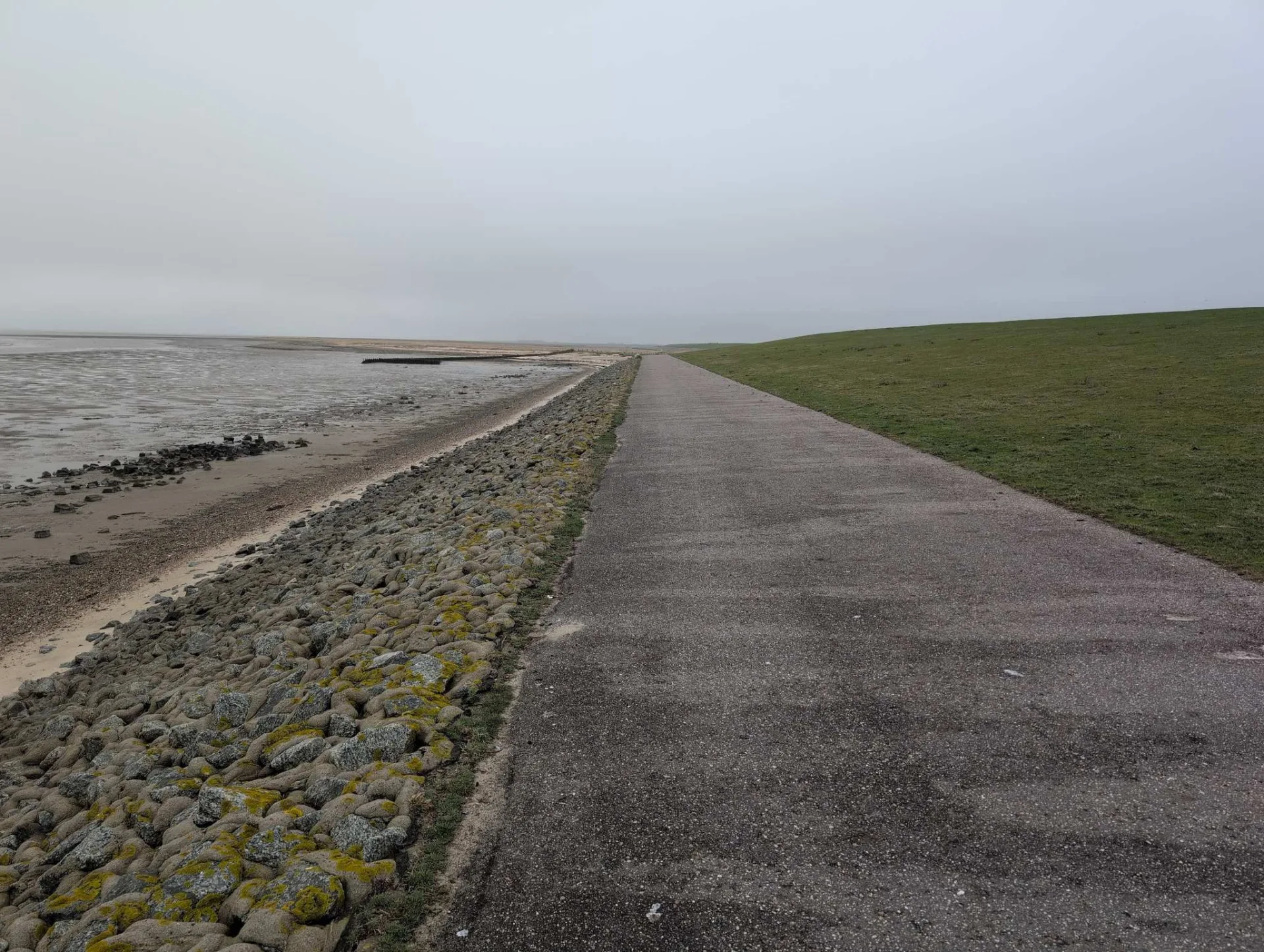 Along the dyke path north of Oldsum, the stone revetment down to the mudflats — all in April haze.