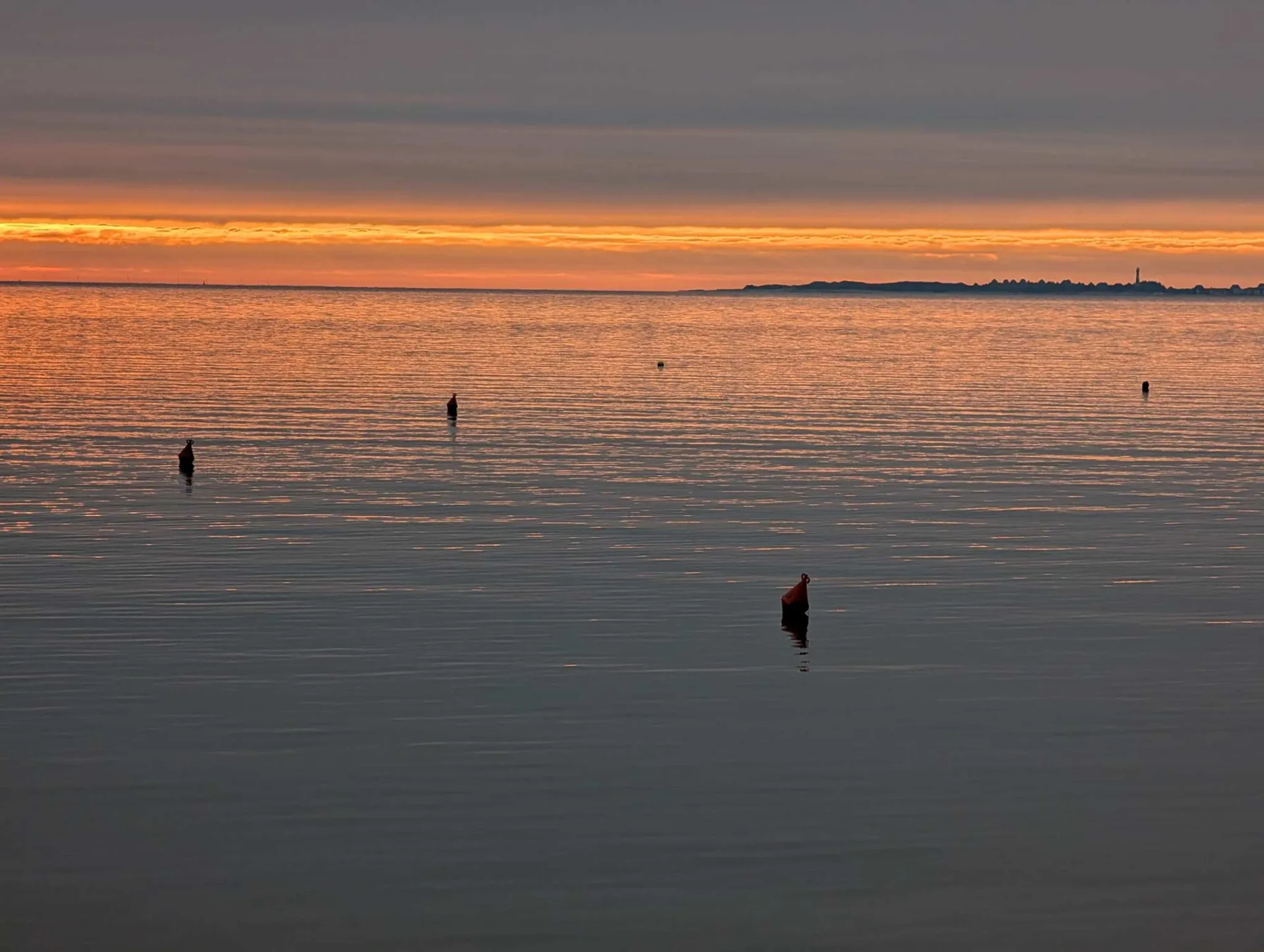 Sunset behind Amrum, birds perched on the channel markers.