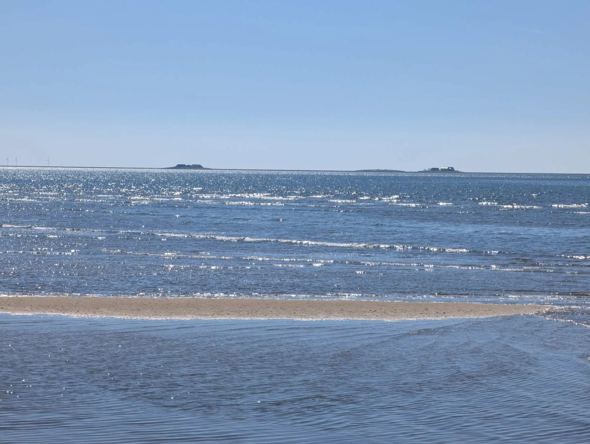 Sunlight glittering on the mudflats off the south beach, low Halligen and distant wind turbines on the horizon.