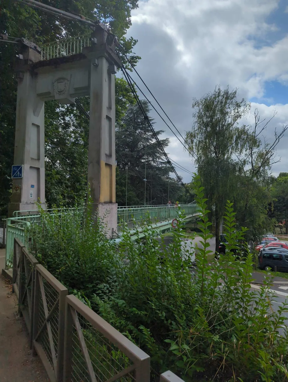An old suspension footbridge, a coat of arms on its pylon, spans the river.