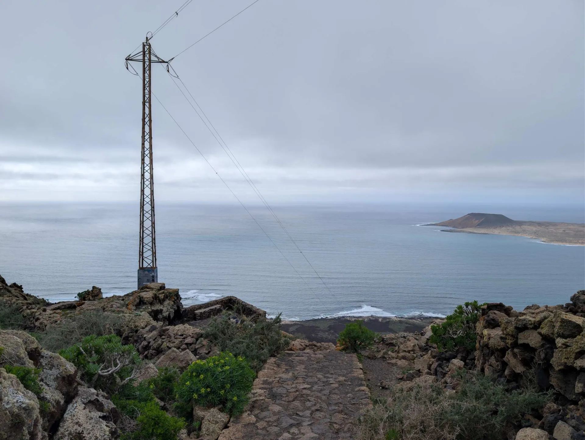 From the edge of the Risco de Famara across to La Graciosa; a power-line mast in the foreground.