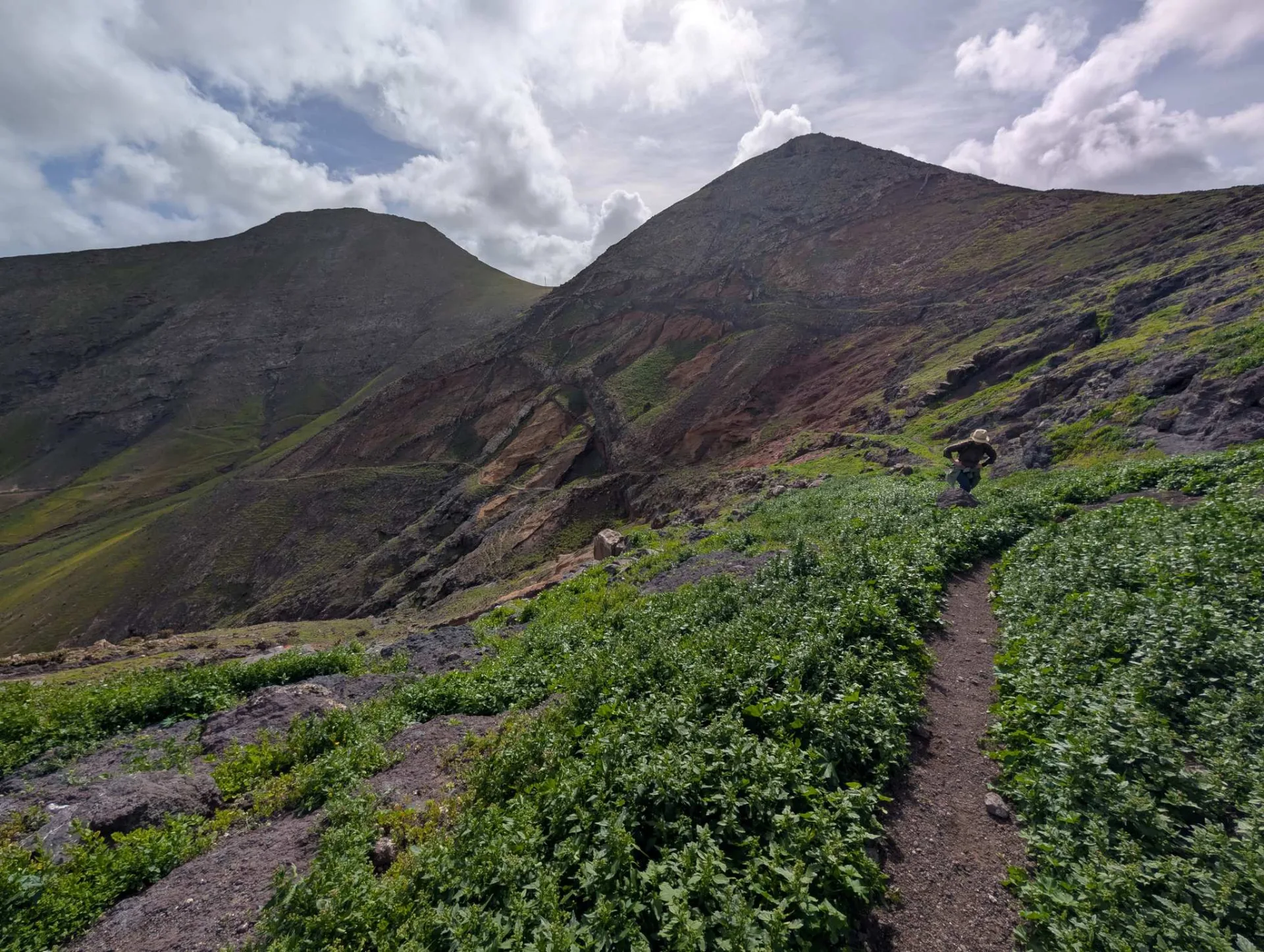 A path winds up to a reddish volcanic cone.
