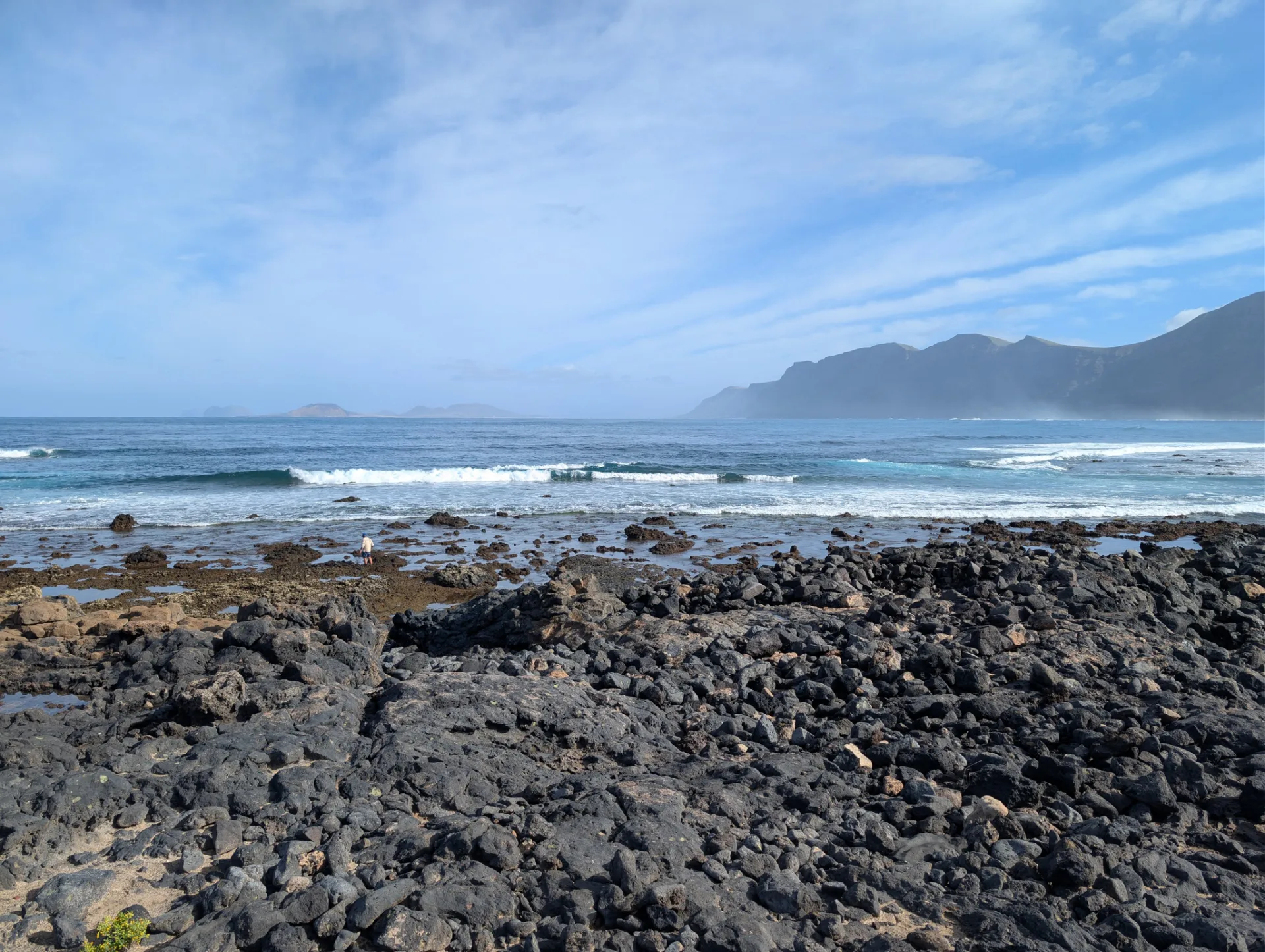 Rugged rocky shore with surf, the Famara massif behind.