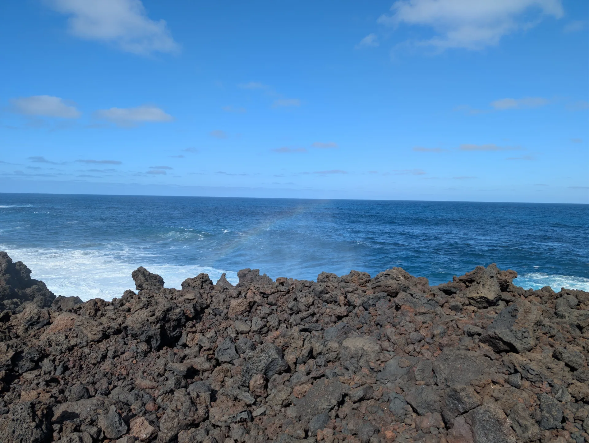 Flat lava ledges at the shore, the wide sea beyond.